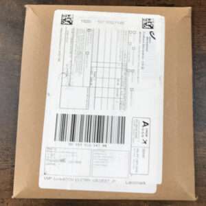 Brown cardboard package with a white shipping label attached, featuring a large barcode and various printed fields visible on the label.