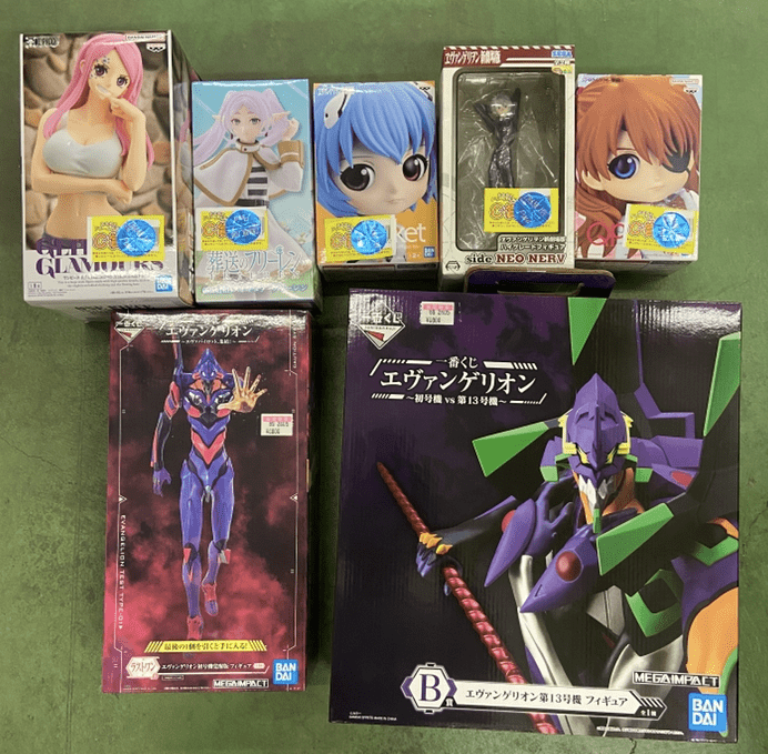 Ver Fotos Recientes 295 - Articulos Japan (post Box Japan) Assortment of boxed anime figures arranged on a green floor, including pink-haired and blue-haired characters among smaller boxes and large Evangelion-model boxes on the bottom row. Articulos Japan (Post Box Japan)