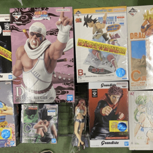 Assorted boxed anime action figures laid on a green surface, including Dragon Ball Z and Grandista boxes with colorful character art.