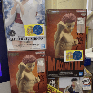Stack of anime figure boxes on a store shelf, featuring a blue-haired character on the left and a muscular character on the right with price stickers.