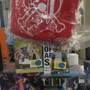 Red square bag with white pirate skull-and-crossbones design placed above collectible figure boxes on a display shelf.