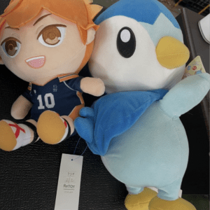 Two plush toys lie on a dark surface: an orange-haired basketball player with jersey number 10 beside a blue penguin plush with yellow beak and feet, tag visible  Articulos Japan (Post Box Japan)