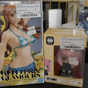 Two boxed anime figures on a store shelf: a tall Glitter & Glamours bikini figure on the left and a SPY×FAMILY Anya Forger figure in a yellow box on the right, both with price tags.