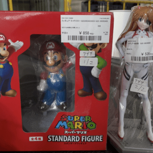 Red Super Mario Standard Figure box with Mario figure visible through the window; a tall wrapped anime figure with price labels stands beside it.