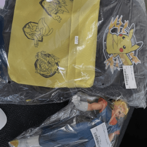 Yellow zippered pouch with black line drawings of cartoon characters, resting on a clear plastic bag beside a black bag with a Pikachu graphic in bold colors (Pokémon-themed). This is an image of toy items still in packaging.