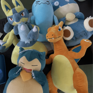 Colorful cluster of plush dragon/dinosaur toys (blue, teal, yellow, orange) piled on a table.