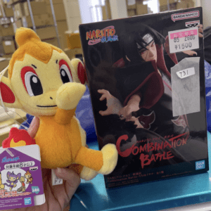 Soft Charmander plush held beside a Naruto: Combination Battle box on a store counter.