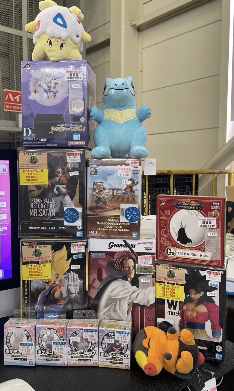 Ver Fotos Recientes 336 - Articulos Japan (post Box Japan) Colorful toy display: large blue Charizard-like figure atop boxes with Dragon Ball figures and plush characters nearby in a store window display. Articulos Japan (Post Box Japan)
