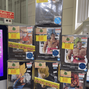 Stack of Dragon Ball action figure boxes on a retail display, featuring characters like Goku and Vegeta with bright yellow price stickers.