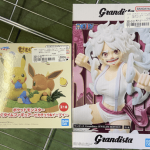 Two boxed collectible figures: Pikachu and Eevee from Pokémon on the left, and a Grandista Jewelry Bonney figure on the right on a metal grid surface.  Articulos Japan (Post Box Japan)