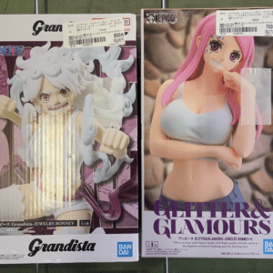 Two boxed anime figures: left a white-haired action-stance figure in a Grandista package; right a pink-haired woman in a white crop top with crossed arms in a Glitter&Glamours box.