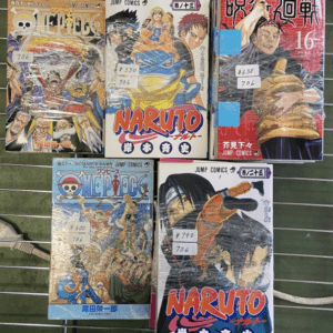 Six Japanese manga volumes in plastic wrap on a metal rack, with visible titles like One Piece and Naruto on display in a shop.