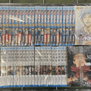 Row of blue-spined manga volumes on a wire rack, mostly uniform with numbered spines and a large cover on the right showing a smiling character.