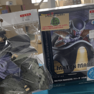 Plastic-wrapped Naruto-style action figure with long black hair next to a Dragon Ball Z Match Makers box on a store shelf outside the packaging area.