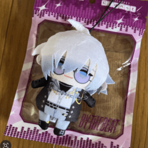 Small plush keychain figure with white hair and purple eyes, wearing a black-and-white outfit, enclosed in pink packaging on a wooden surface.
