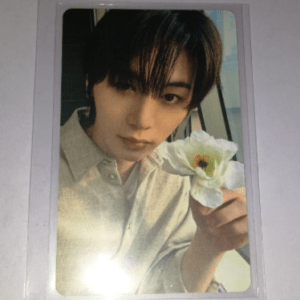 Close-up portrait of a young man in a beige shirt holding a white flower toward the camera.