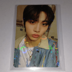 Polaroid-style portrait of a young person with dark hair making a pouty face, wearing a light denim jacket and layered necklaces.