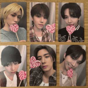 Six photo cards arranged on a wooden surface, each showing a young man holding a pink swirled heart lollipop near his mouth or cheek.
