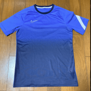 Blue gradient Nike athletic shirt laid flat on a wooden floor with a white Nike swoosh on the chest.