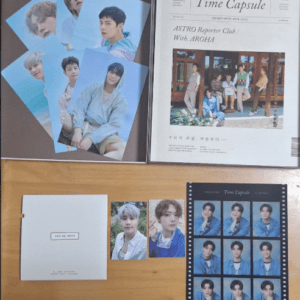 K-pop photo cards and a Time Capsule newspaper spread on a wooden table with a small white booklet nearby.
