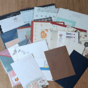 A scattered assortment of decorative envelopes and letter papers on a wooden floor.