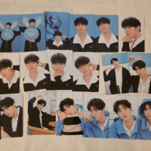 Collection of glossy photocard cards laid on a light surface, featuring male performers in various poses and outfits.