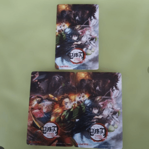 Two Demon Slayer trading cards laid on a green surface, showing colorful action-art of battle-ready anime characters.