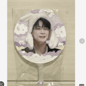 Round handheld fan showing a smiling person wearing a plush bunny-ear hood, set against pastel purple clouds and stars design (in plastic packaging)