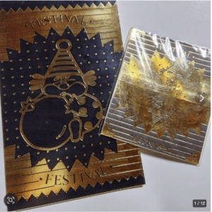 Gold foil festival card with a starburst design and a cartoon character emblem.