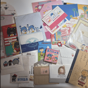 A pile of colorful envelopes, cards, and stationery featuring cute cartoon characters and vintage designs, scattered in a cluttered arrangement.