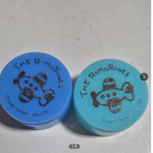 Two plastic caps in blue and light blue featuring a black cartoon dog logo and the text 'THE RUNABOUTS'.