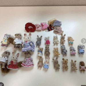 Collection of small plush animals arranged in rows on a white surface, including rabbits, bears, and cats in pastel outfits.