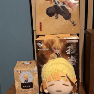 Plush anime figure with yellow hair and orange outfit sitting on a wooden shelf in front of boxed figures and a poster.