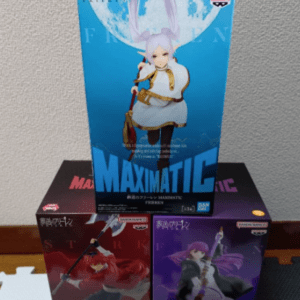 Stack of three Maximatic action figure boxes on the floor: blue top box featuring a white-haired character, red and purple boxes beneath.