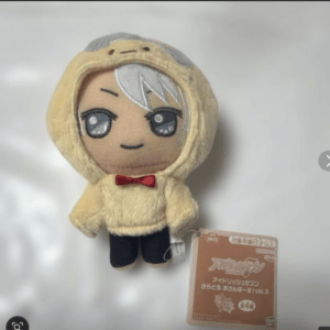 Plush doll in a beige hooded outfit with a red bow tie and dark pants on a white surface, tag attached.