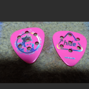 Two pink guitar picks with multiple holes resting on a rough stone surface.