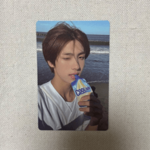 Young man at the beach holding and licking a blue-and-white Coolish ice cream pouch on a sunny day.