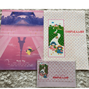 Colorful pastel stationery set on a fuzzy rug: a large pink poster with a bridge scene and a climber, plus a white Simple Lands booklet and a small pink card with similar art.