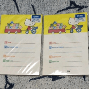 Two small Hello Kitty-themed notebooks with yellow tops showing form fields for name, new address, telephone, and message on a light page, placed on a patterned rug.