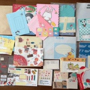 A collage of colorful kawaii letters, envelopes, notepads, and gift cards with cartoon characters and patterns scattered on a wooden surface, showing assorted stationery items for writing and crafts.