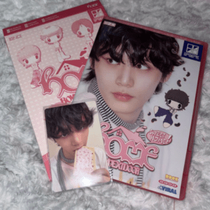 Pink K-pop merchandise: two DVD/case boxes featuring a young male idol’s portrait, plus a photo card of him eating cake.