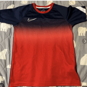 Nike DRI-FIT athletic shirt with navy top fading to red and a dotted gradient pattern on a bedspread backdrop, white swoosh on chest (informative).