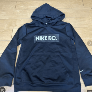 Navy Nike F.C. hoodie laid flat on a wooden floor, showing the front pouch pocket and bold NIKE F.C. logo across the chest.