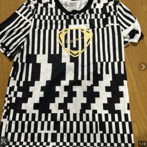 Black and white pixel-patterned T-shirt with a gold shield logo and a Nike swoosh at the chest area (Dri-Fit tag visible inside collar)