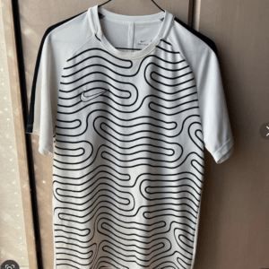 White Nike Dri-FIT t-shirt with a black wavy line pattern hanging on a hanger in a closet.