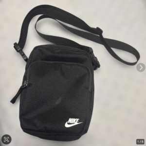 Black Nike crossbody bag with an adjustable strap and front zipper pocket on a light background
