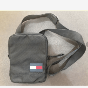 Black compact crossbody bag with an adjustable strap and a small flag patch on the front.