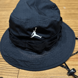 Black bucket hat with a white Jumpman logo on the front, resting on a wooden floor.  Articulos Japan (Post Box Japan)