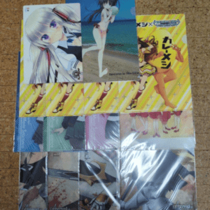 Assorted anime trading cards and postcards laid on a yellow striped box, featuring a beach swimsuit character, a silver-haired girl, and various character art.  Articulos Japan (Post Box Japan)