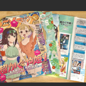Two anime manga magazine covers on a wooden table, showing illustrated girls and bright, bold titles.  Articulos Japan (Post Box Japan)
